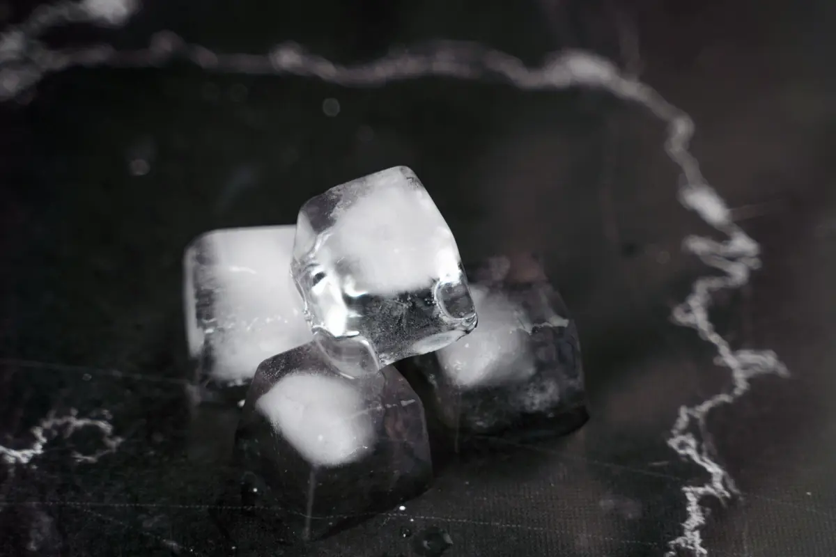 Cubos de gelo com reflexo de água sobre superfície escura